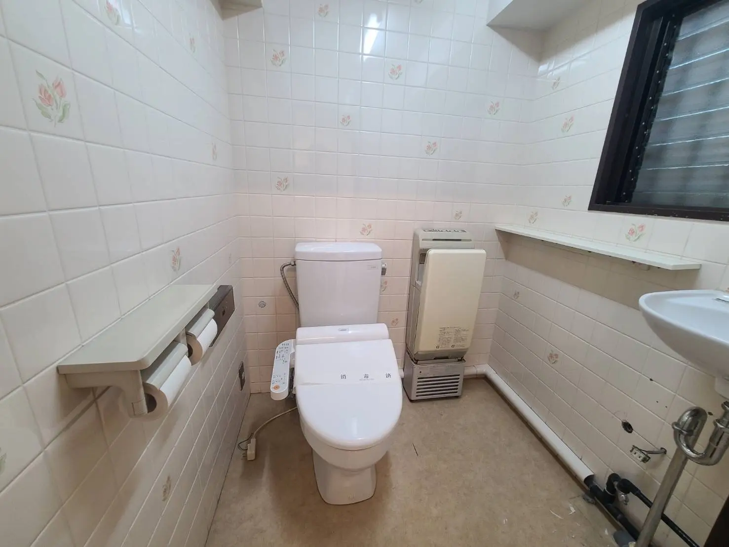 清潔感あるタイル壁のトイレと手洗い器、紙ホルダーとウォシュレット機能付き便座、浴室暖房乾燥機のあるバスルーム