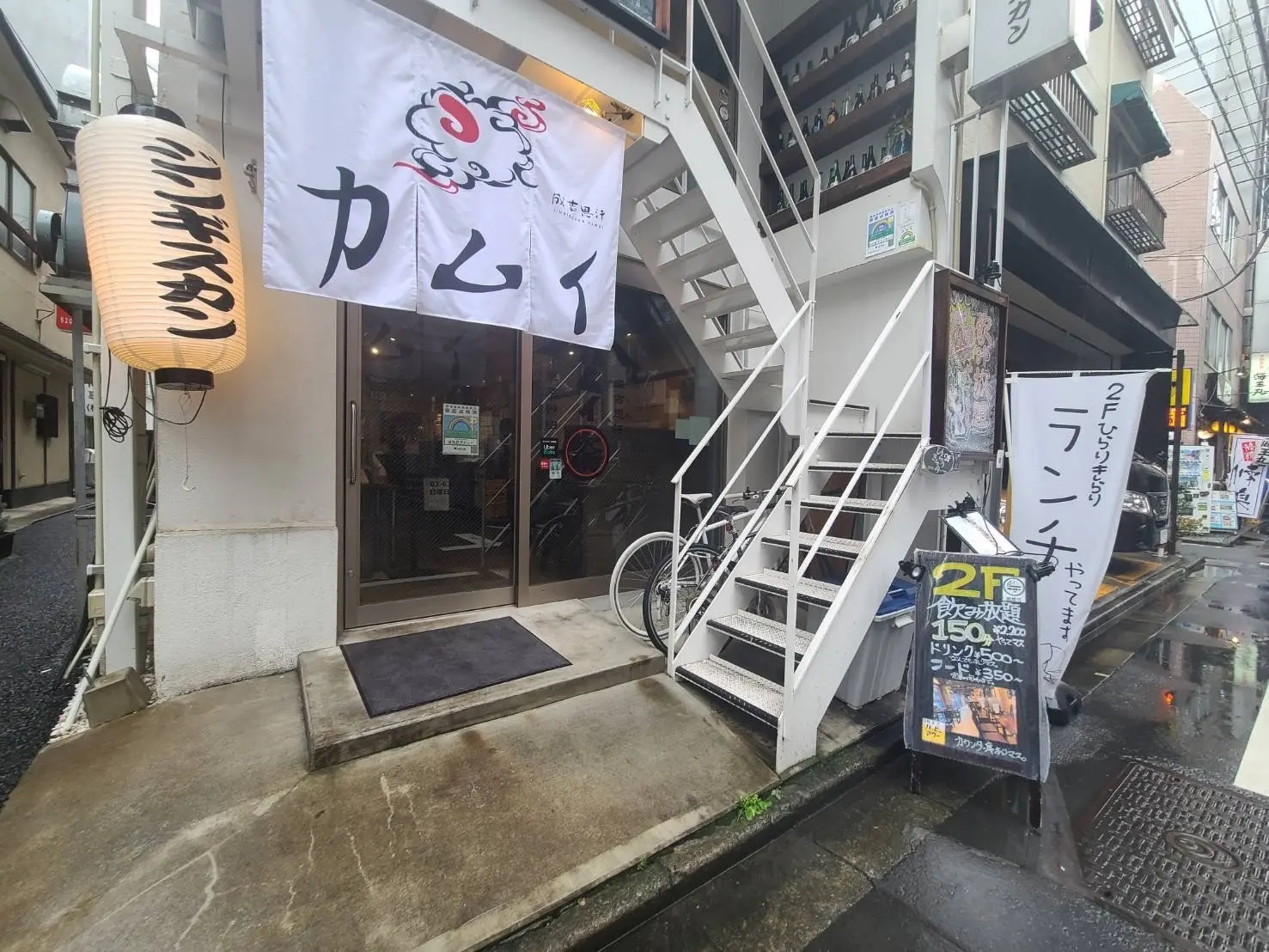 日本の街角にある居酒屋の入り口、暖簾と提灯があり、外階段が特徴的な店舗外観