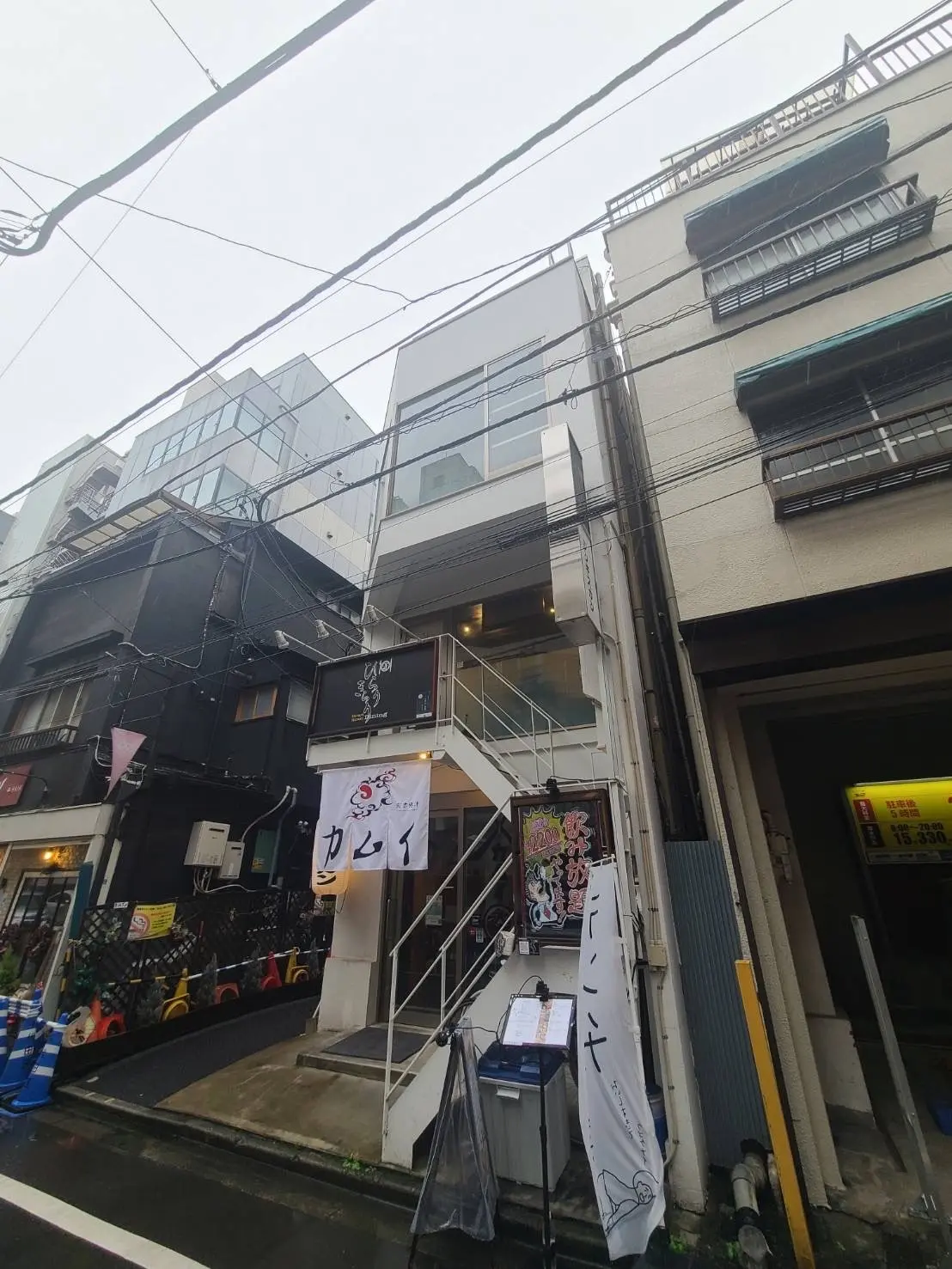 雨の日に撮影された都市風景、見える看板によると和食レストランの入り口、周囲には他の店舗や建物が密集
