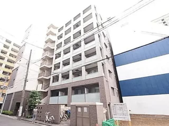 - シンプルでスタイリッシュな外観のマンション、周囲には他の建物と電線が見える都市の風景