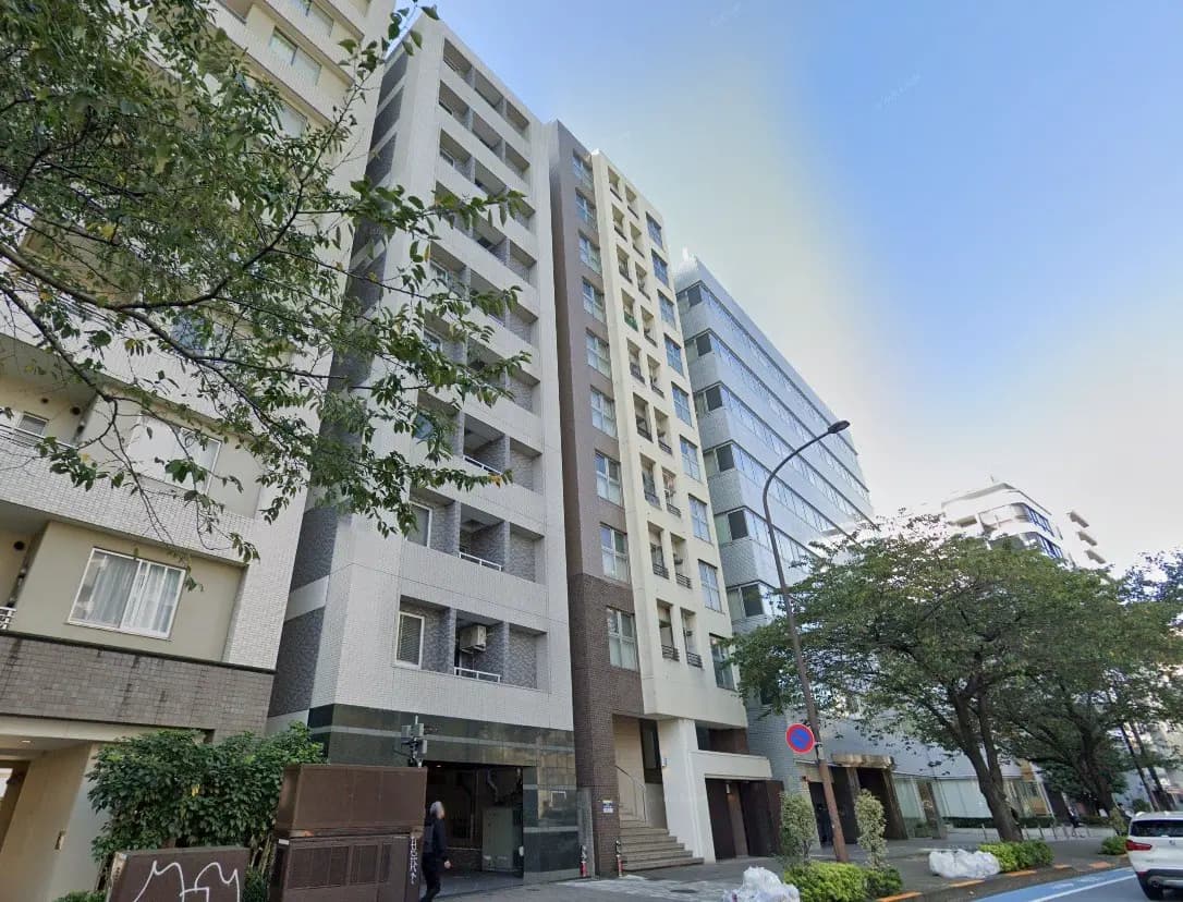 都市の通りにあるモダンなマンションビル、青空と緑豊かな樹木が映える都会の住環境