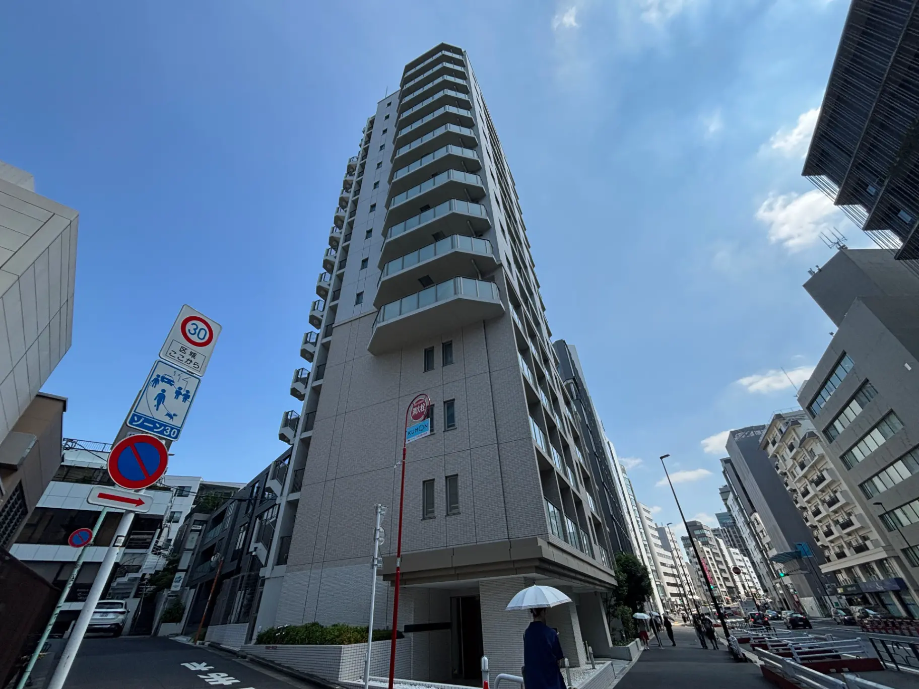 - 高層マンションの外観、明るい青空の下で立つ、周囲には交通標識と歩行者が見える都市風景