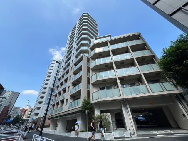 - 高層マンションの外観、近代的なデザインとバルコニーを持つファサード、晴れた青空の下を歩く人々が写っている都市の風景