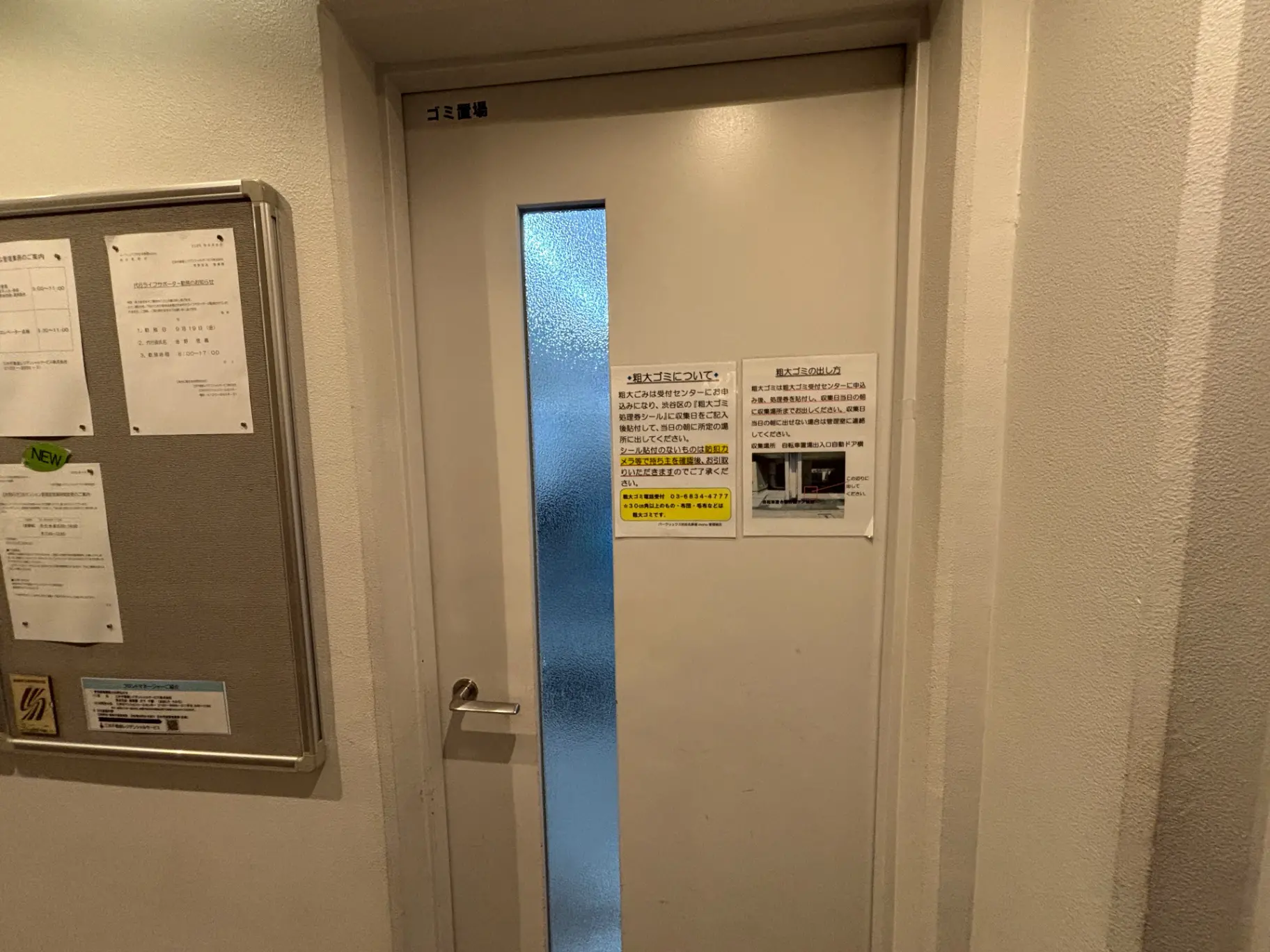 - ゴミ捨て場のドア、透明なガラス窓があり、周囲に掲示物が貼られた壁面の一部が見える部屋の入り口