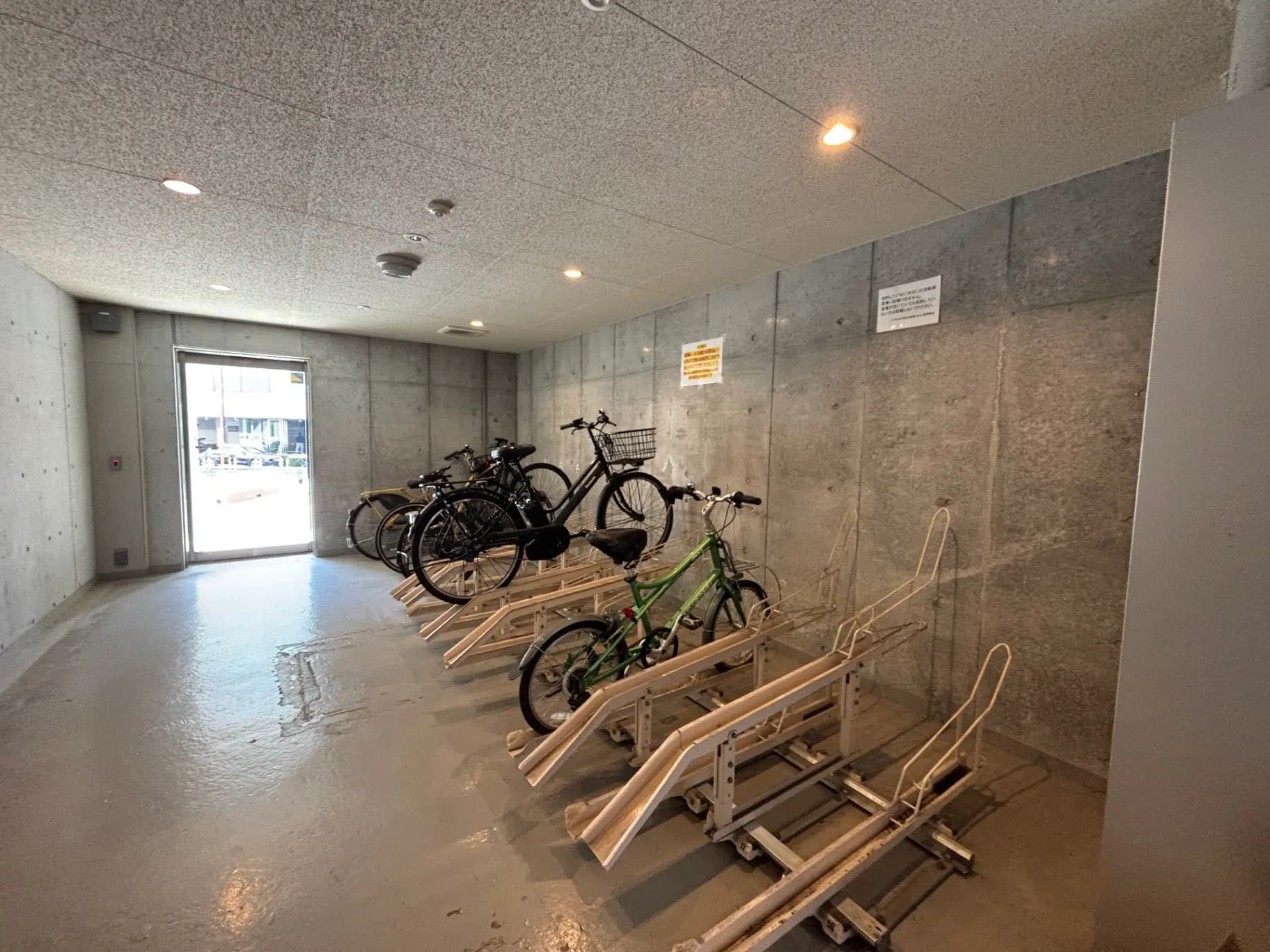 - 自転車用の駐輪場、コンクリートの壁と床、緑色の自転車が目立つ明るいスペース