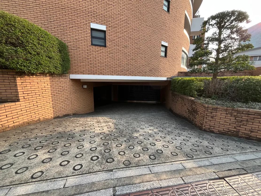 - ブロックレンガの外壁を持つ建物の駐車場エントランス、円形模様の舗装と緑の植栽が特徴的な景観