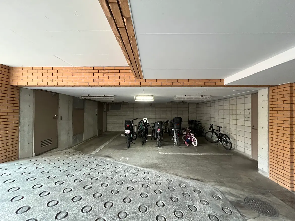 - 自転車置き場の内部、コンクリートの床とレンガの壁が特徴、複数の自転車が並ぶ様子