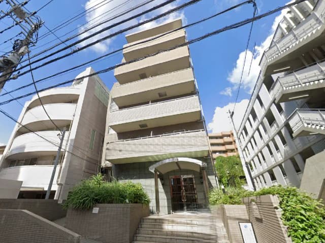 - 都市型マンションの外観、モダンなデザインのエントランスと周囲の建物、晴天に映える青空とのコントラスト