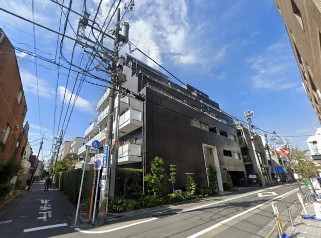 - モダンな外観のマンション、青空と電柱が映える街角の風景、周囲に植栽が見える住宅地の一画