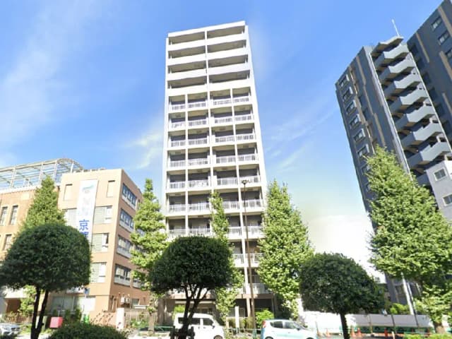 - 都市の高層マンション、青空を背景にした建物、周囲には緑の木々と他のビルが立ち並ぶ景観