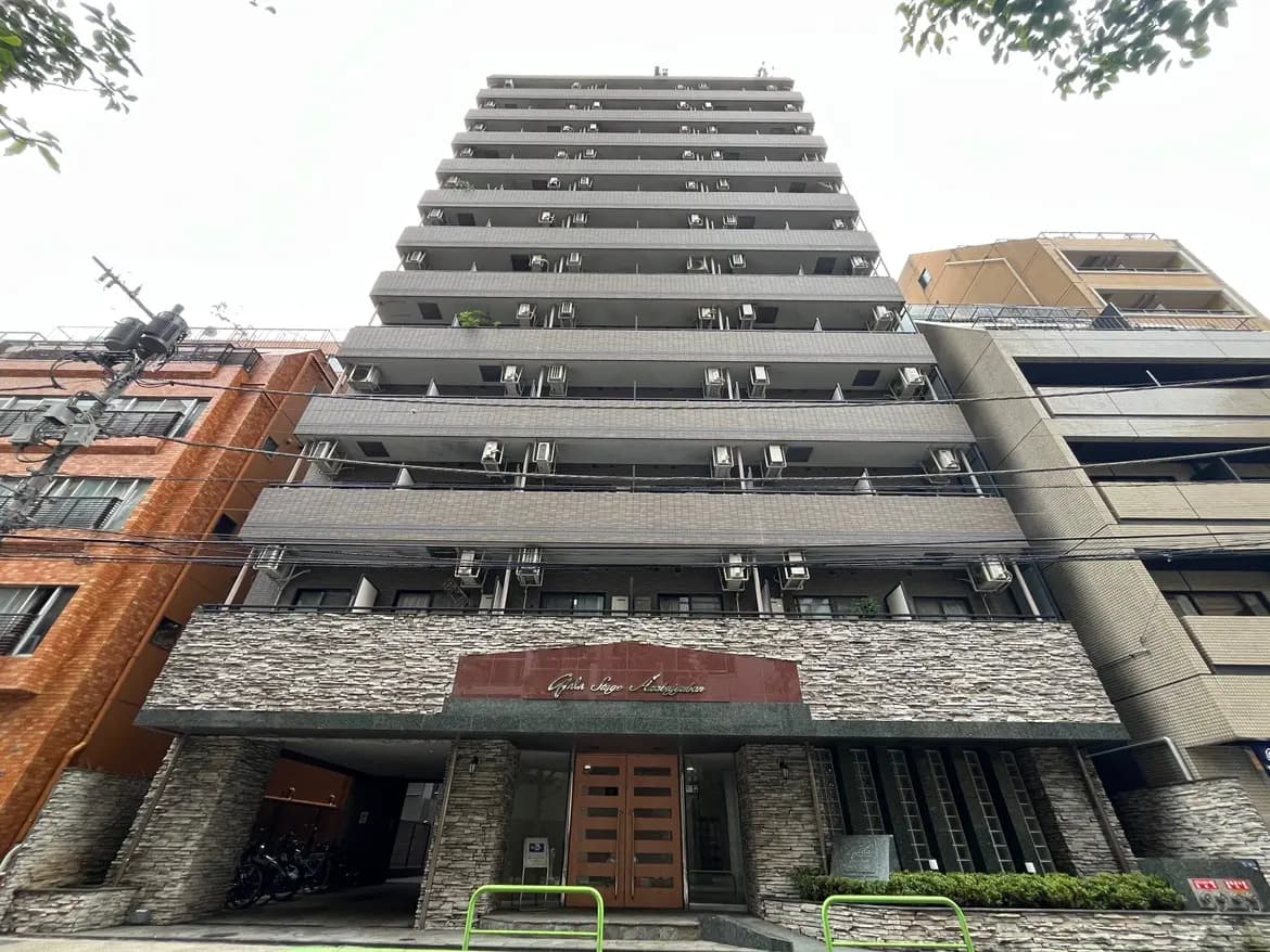 - モダンな外観の10階建てマンション、石材のファサードと多くのエアコンユニット、隣にはレンガ造りのビルが立ち並ぶ景観