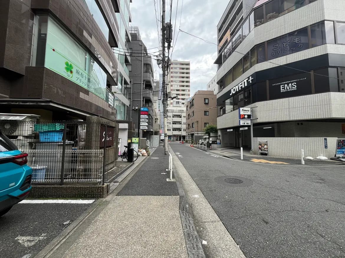 - 都市部の静かな通り、商業ビルと住宅が並ぶ風景、歩道にはゴミが置かれた様子