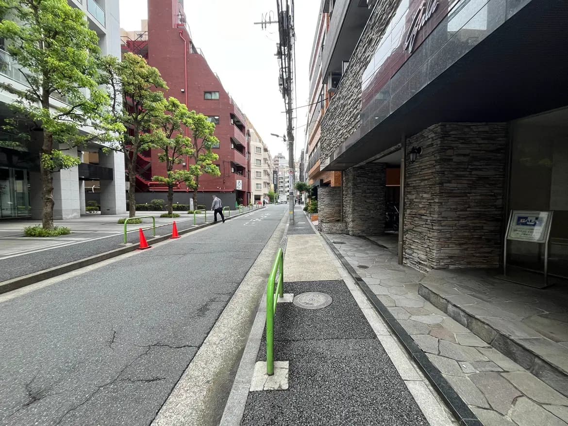- 都会的な風景の歩道、緑の植栽と舗装された道路、赤い交通コーンと近くの建物が並ぶ静かな通り