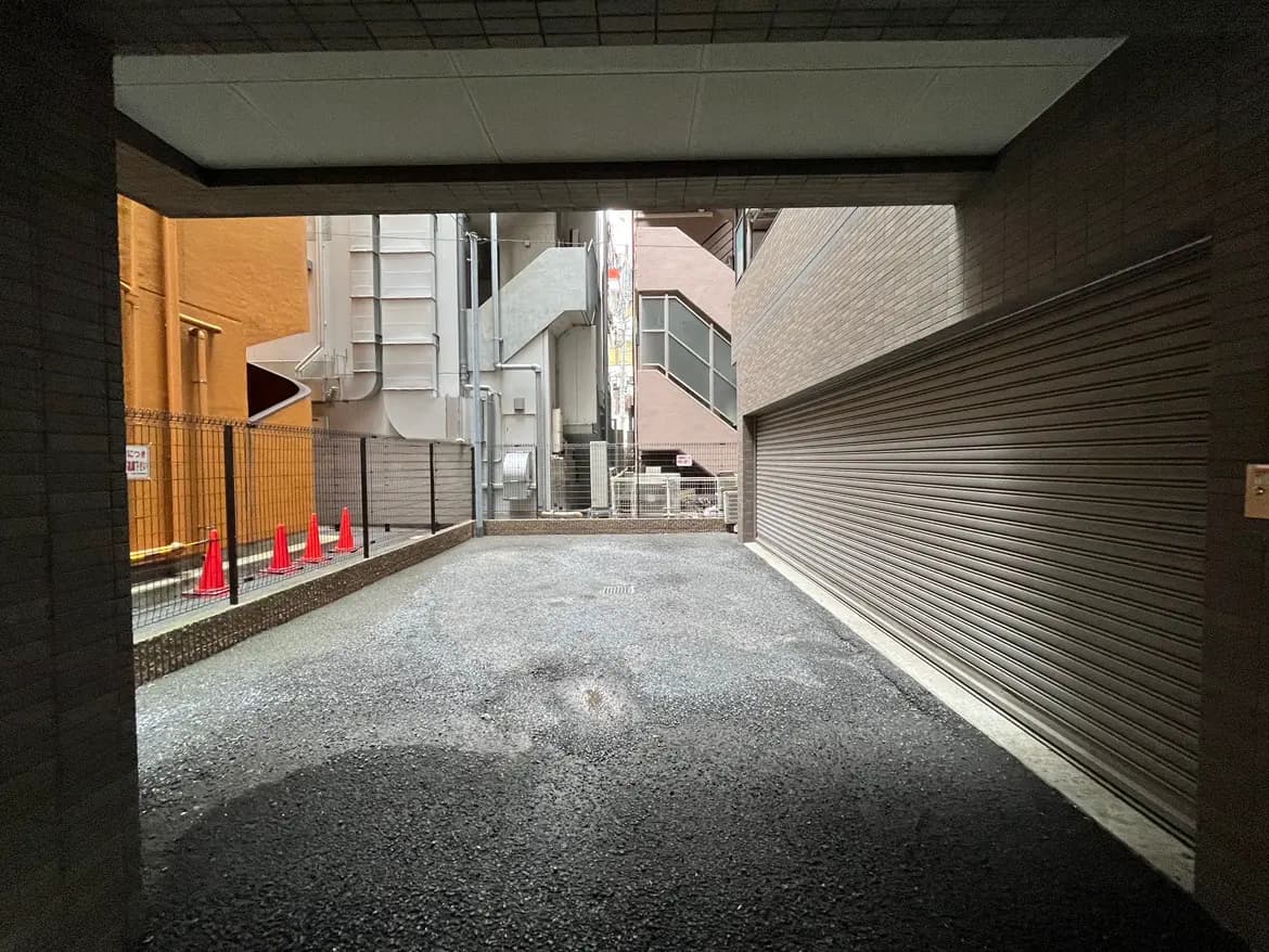 - 駐車場の入口、周囲に赤いコーンが並び、隣接する建物の壁が見えるアングルの風景