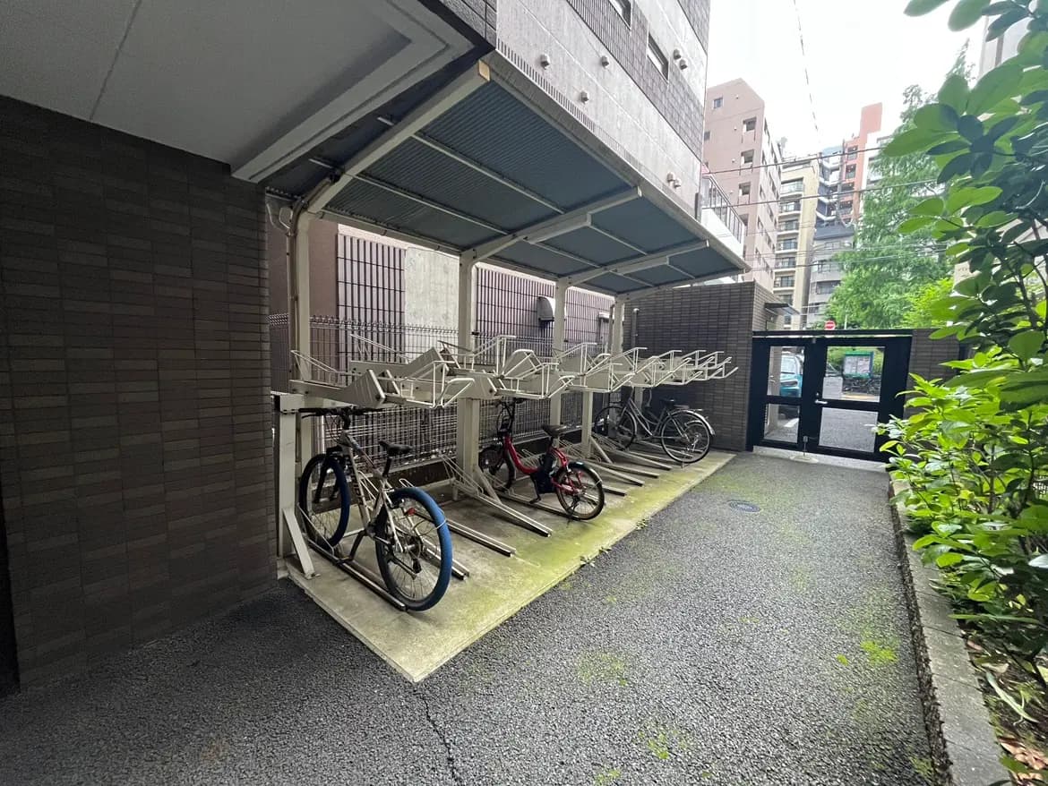 - 屋根付きの自転車置き場、複数の自転車が駐輪されている風景、周囲には建物が立ち並ぶ都市の一角