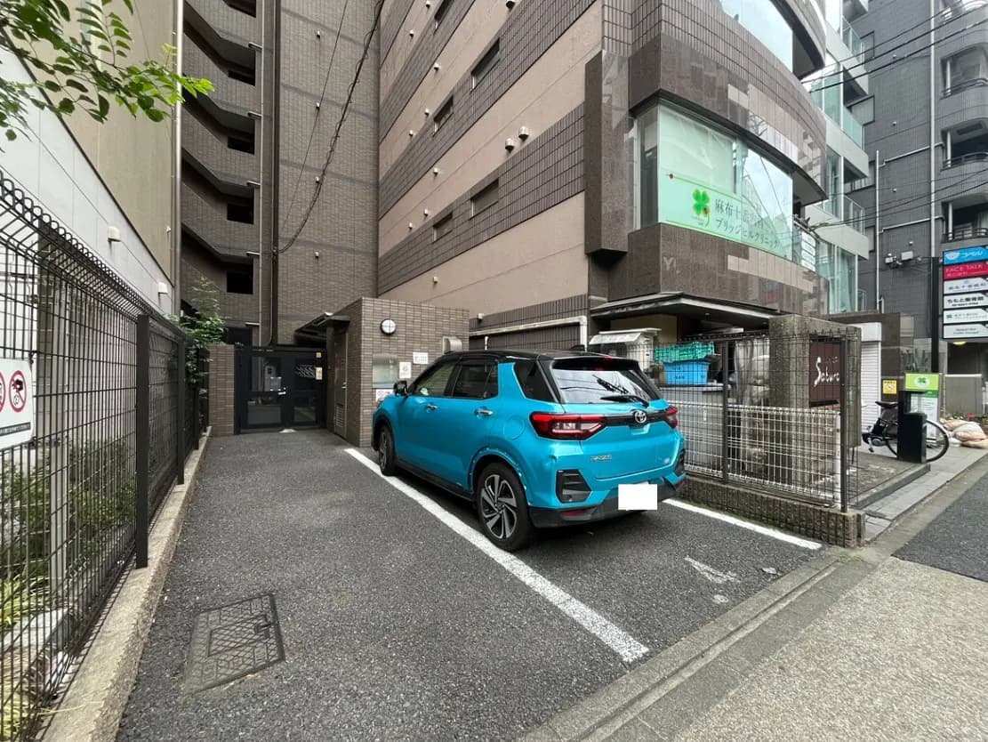 - アパートの駐車場に停まる青い車と、周囲に立つ近代的な建物の外観