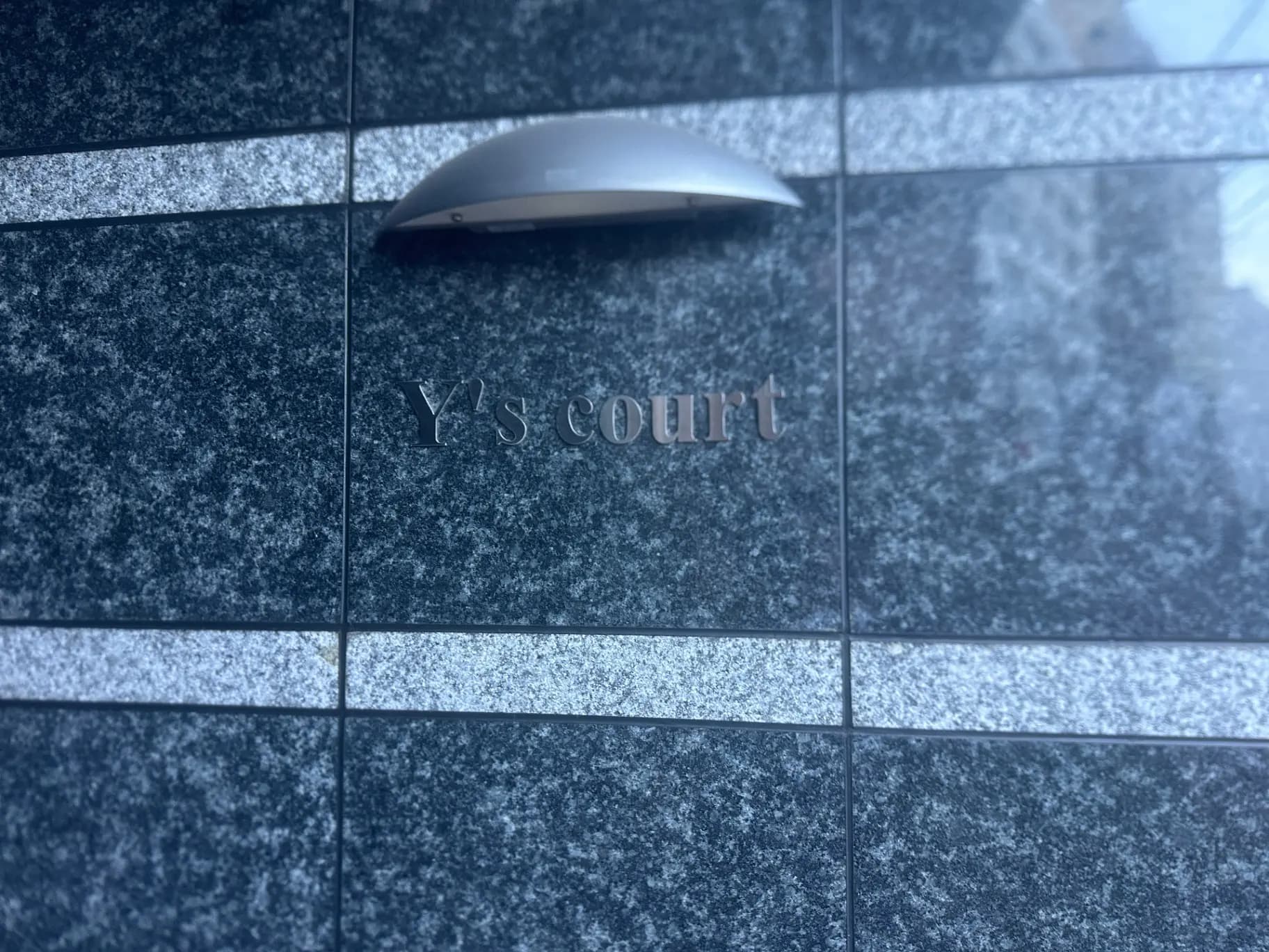 建物の外壁に取り付けられたモダンなデザインの照明器具と「Y's court」と刻まれたサイン