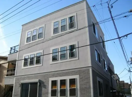 - モダンなデザインの3階建てアパートメント、白とグレーの外壁、複数の窓と電線が交差する街中の風景