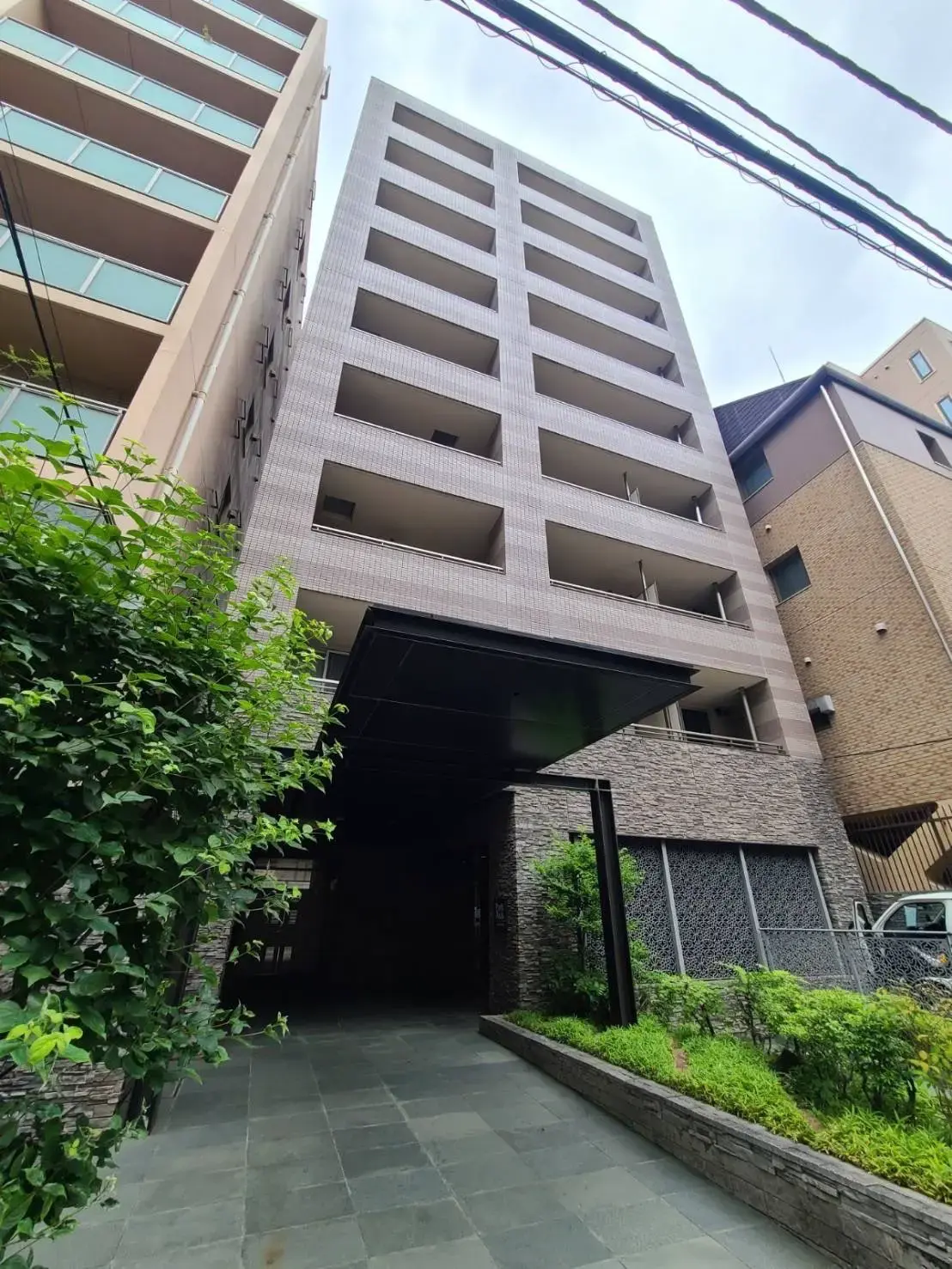 モダンな外観のマンションビル、緑豊かなエントランスアプローチ
