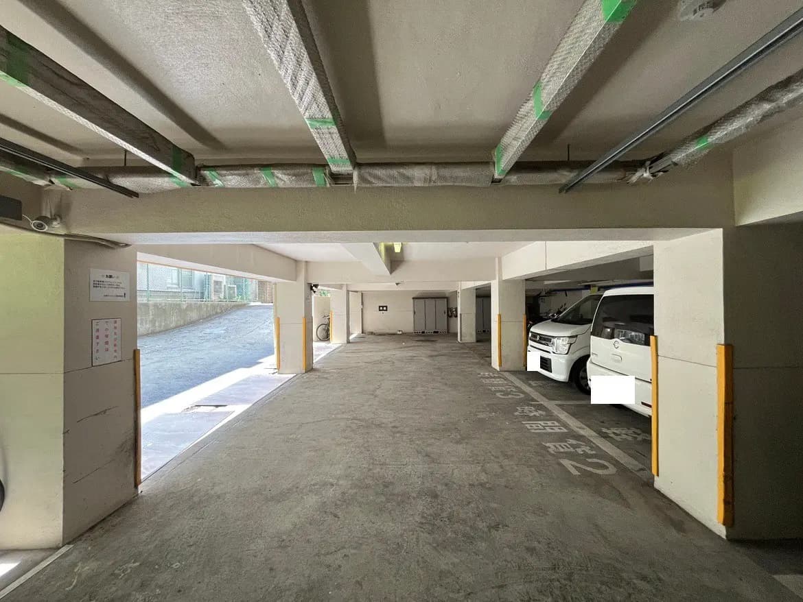 - 明るい室内駐車場の風景、駐車スペースが並び、自然光が差し込むエリア、車両が停まっている様子