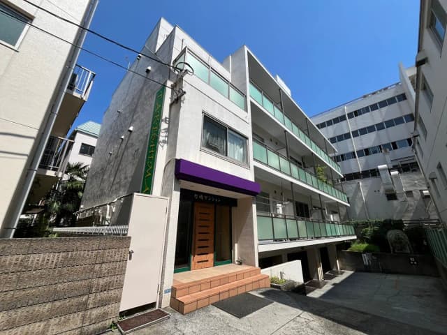 - 青空の下、紫色の屋根が特徴的な竹島マンションの外観と、周囲の住宅が並ぶ風景