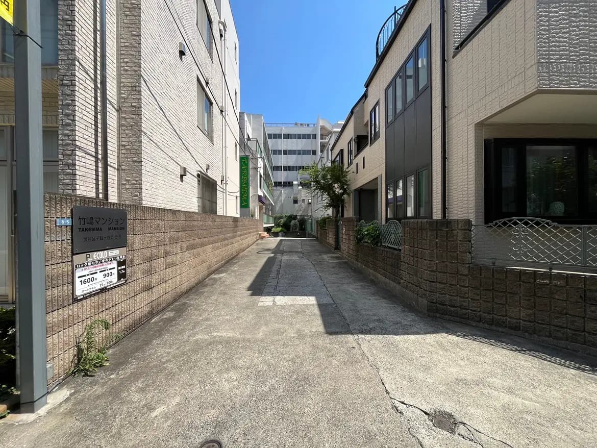 - 竹嶋マンションの外観、周囲に住宅が並ぶ静かな路地、青空が広がる日中の風景