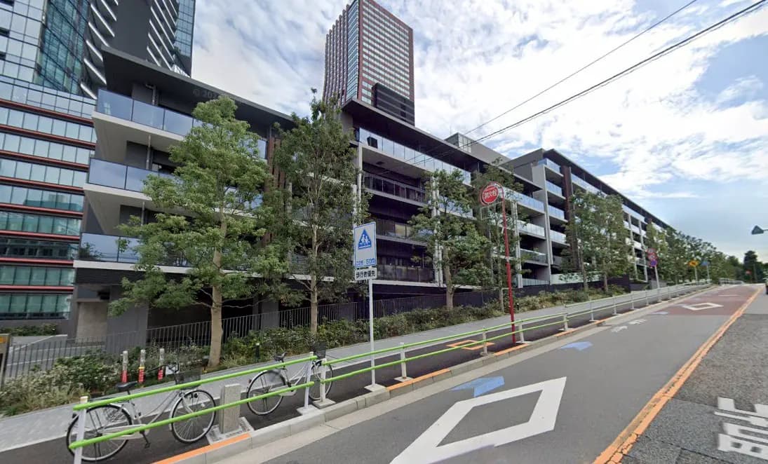- モダンな外観の集合住宅、緑豊かな植栽と自転車置き場が整備された風景、空に浮かぶ雲とのコントラスト