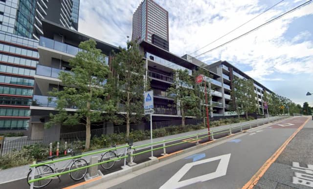 - モダンな外観の集合住宅、緑豊かな植栽と自転車置き場が整備された風景、空に浮かぶ雲とのコントラスト