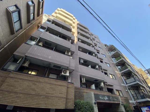 - 都市型マンションの外観、レンガ調の外壁とバルコニー、青空の下で撮影された高層ビルの様子