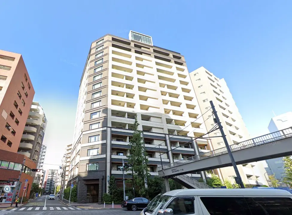 都市の景観に溶け込むモダンなマンション、晴れた日の青空、歩道橋と街路樹が見える外観