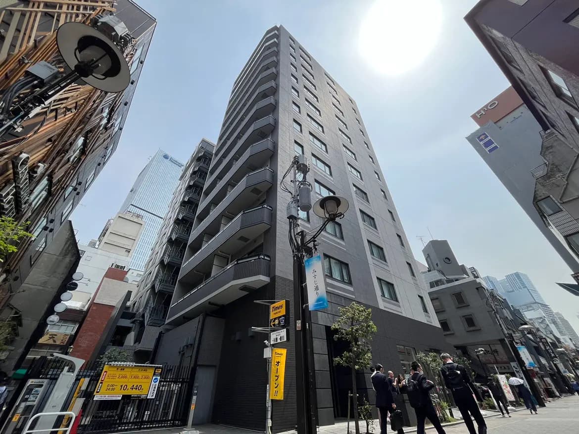 - 都市のビル群の中に立つ近代的なマンション、青空の下で人々が行き交う賑やかな街並み