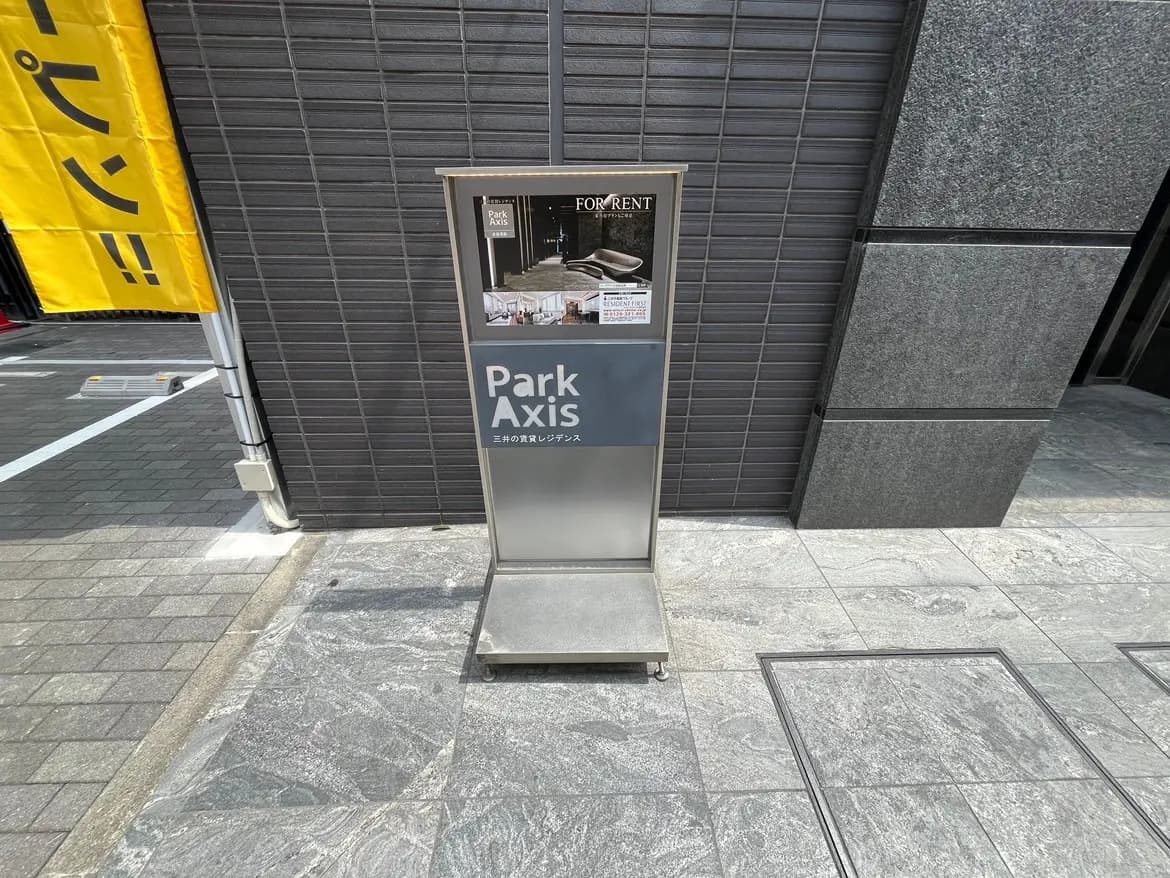 - 「Park Axis」という文字が書かれた賃貸物件の案内板、黒いタイルの壁の前に設置されたスタイリッシュなデザインの看板。