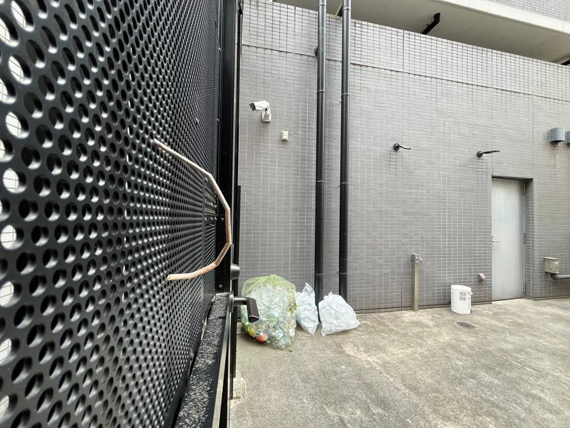 - 黒い金属製のフェンスと灰色のタイル壁、収集されたゴミ袋が配置された裏庭の風景