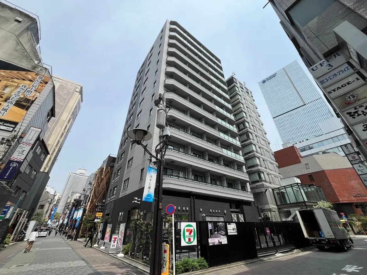 - 高層ビルが立ち並ぶ繁華街の風景、手前にはセブンイレブンの店舗と商業施設が見える都市のイメージ