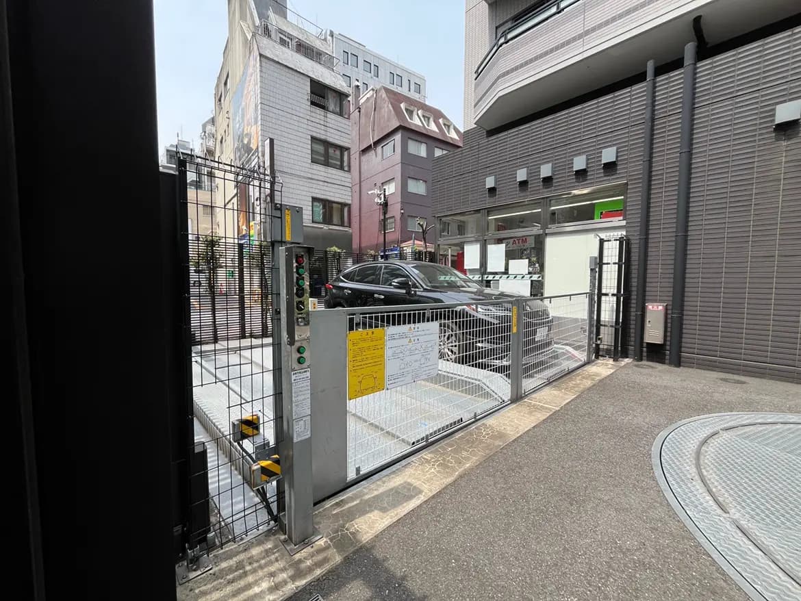 - 都心の駐車場入口、ゲートと操作パネル、隣に店舗がある街の風景
