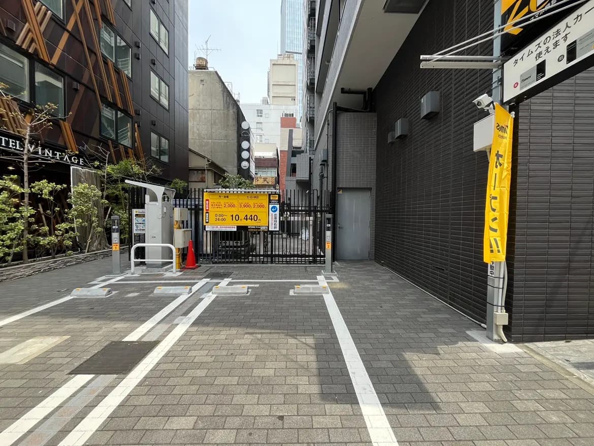 - 都心の駐車場入り口、料金案内の看板と自動車用ゲート、周囲に建物が立ち並ぶ風景