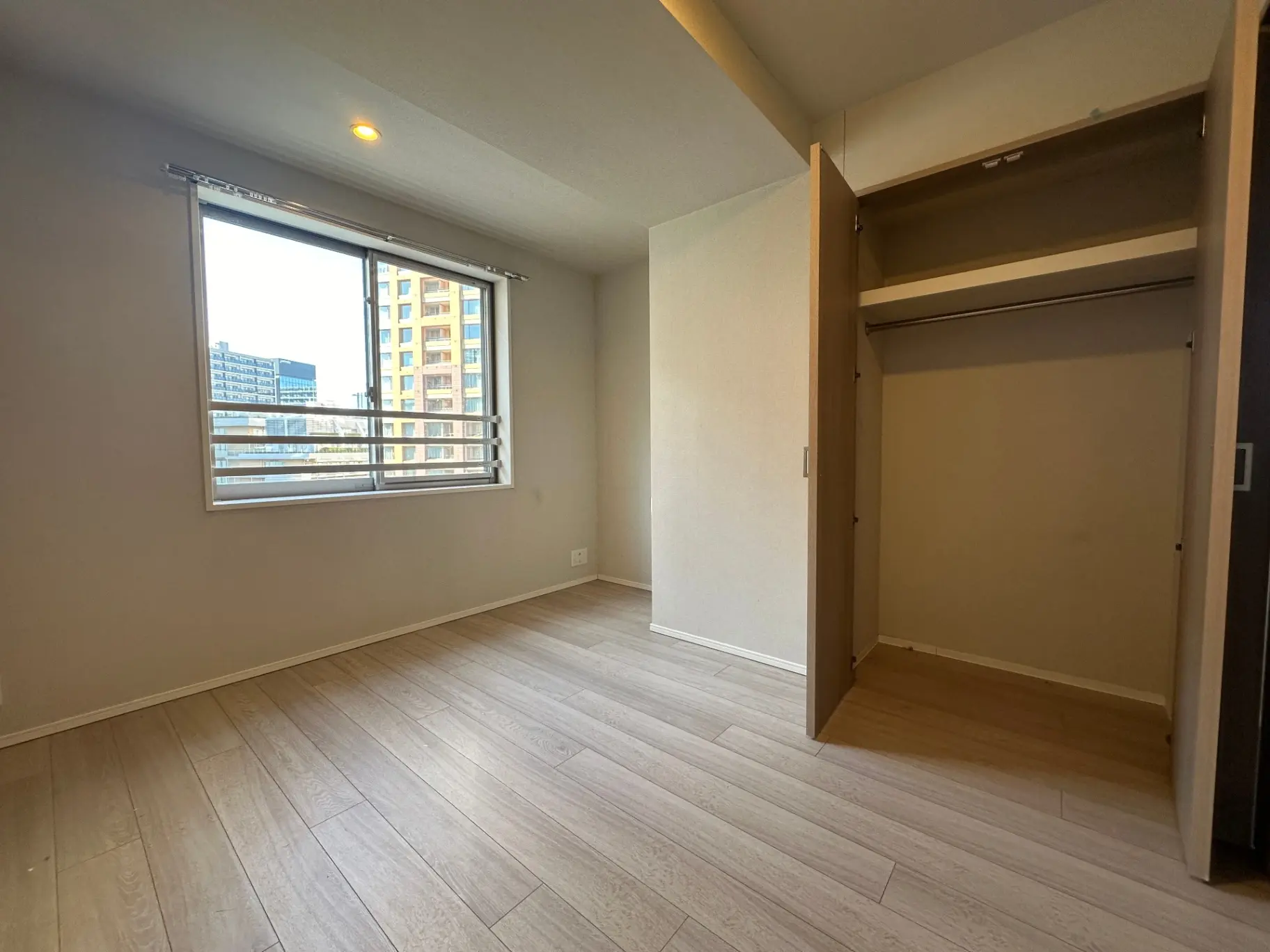 明るい自然光が差し込むシンプルなデザインの空き部屋、木製フローリングと大きな窓、開いたクローゼットのあるインテリア