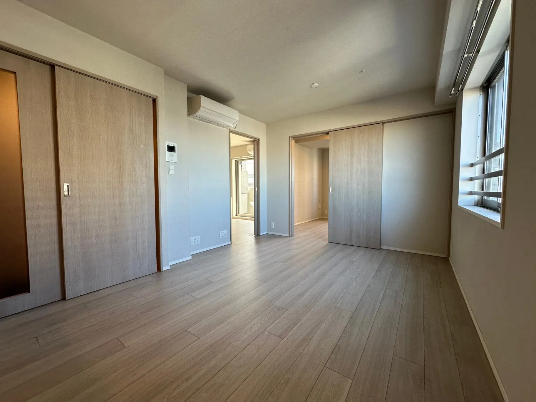 明るい空間と木目調のフローリングが特徴的な新築マンションの室内、エアコンとクローゼットが備わる