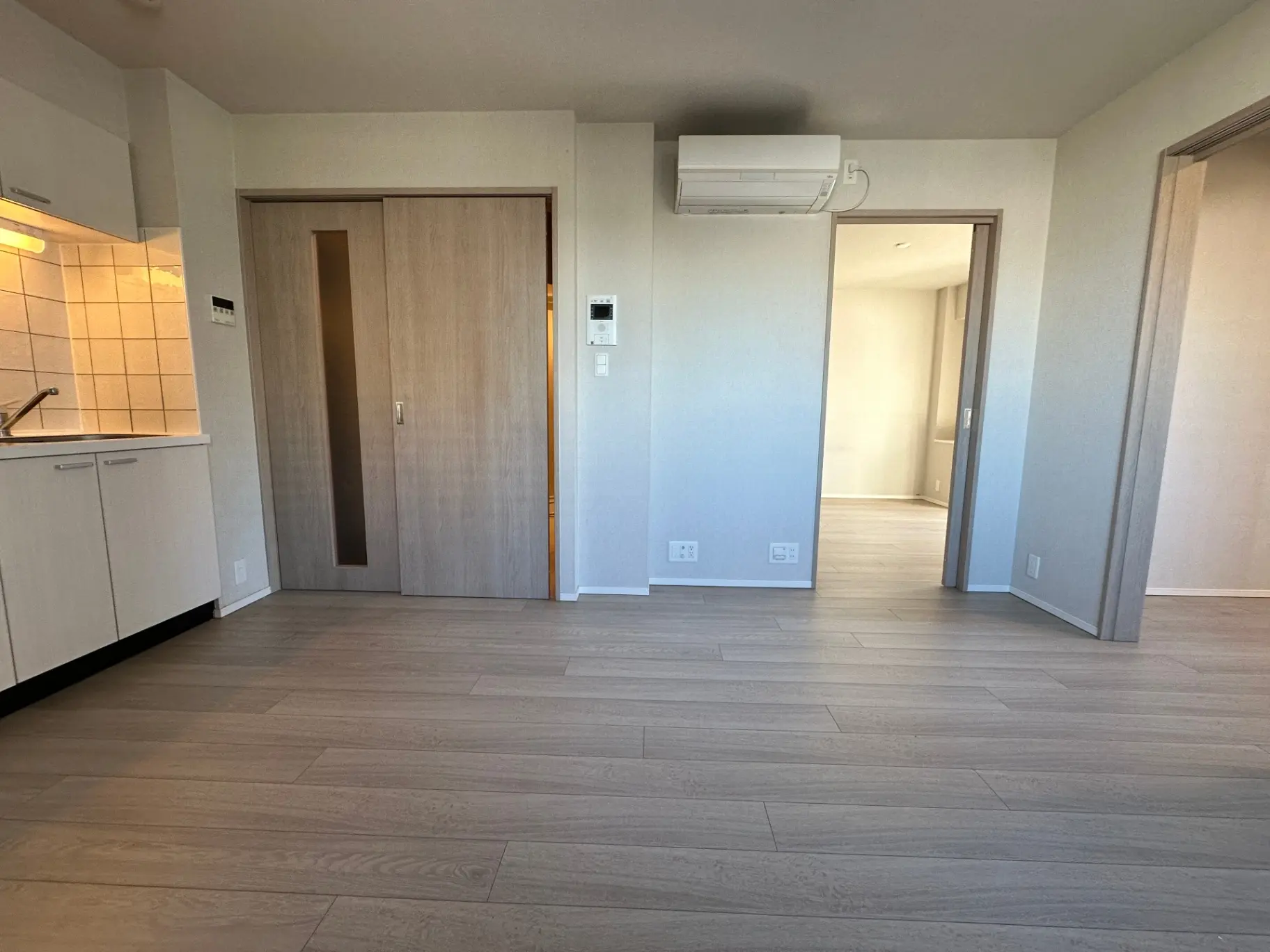 シンプルなデザインの新築マンション内観、キッチンとリビングの間に木目調の扉、ナチュラルな色合いのフローリング