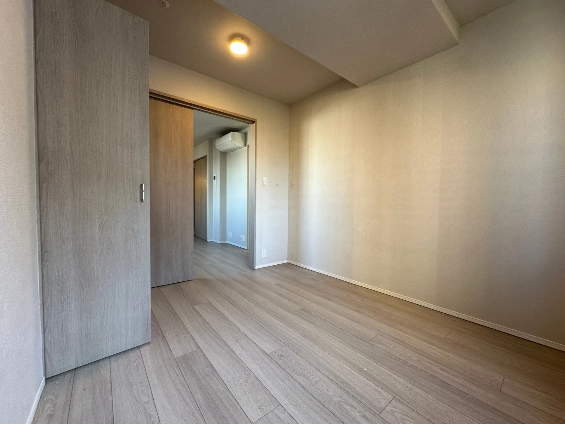 シンプルでモダンな内装の部屋、木目調フローリング、白い壁、ダウンライトが特徴の空間