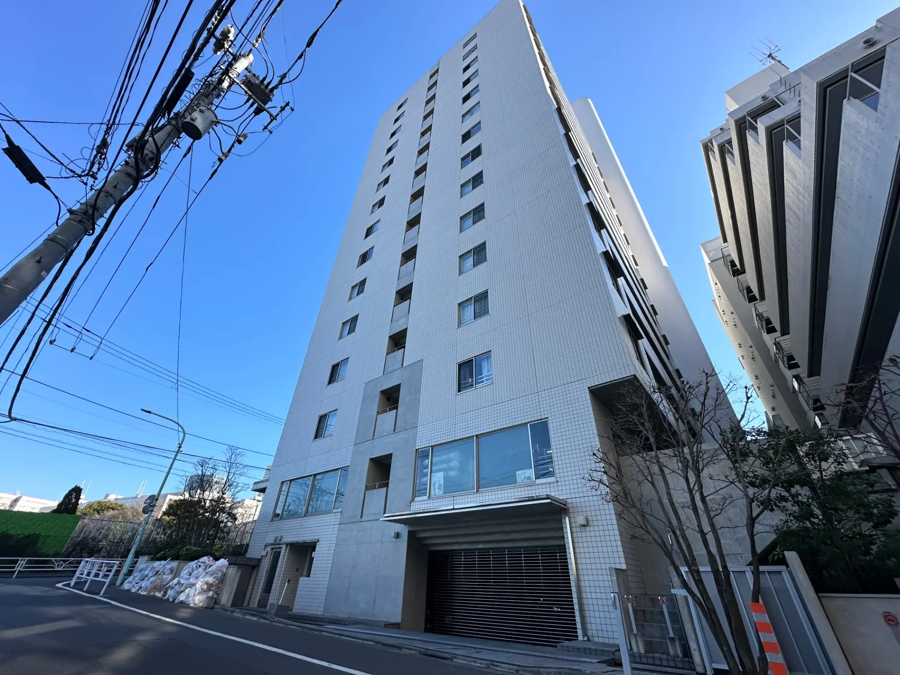 現代的なマンションの外観、青空のもと都市の建物、歩道橋と電柱が見える風景