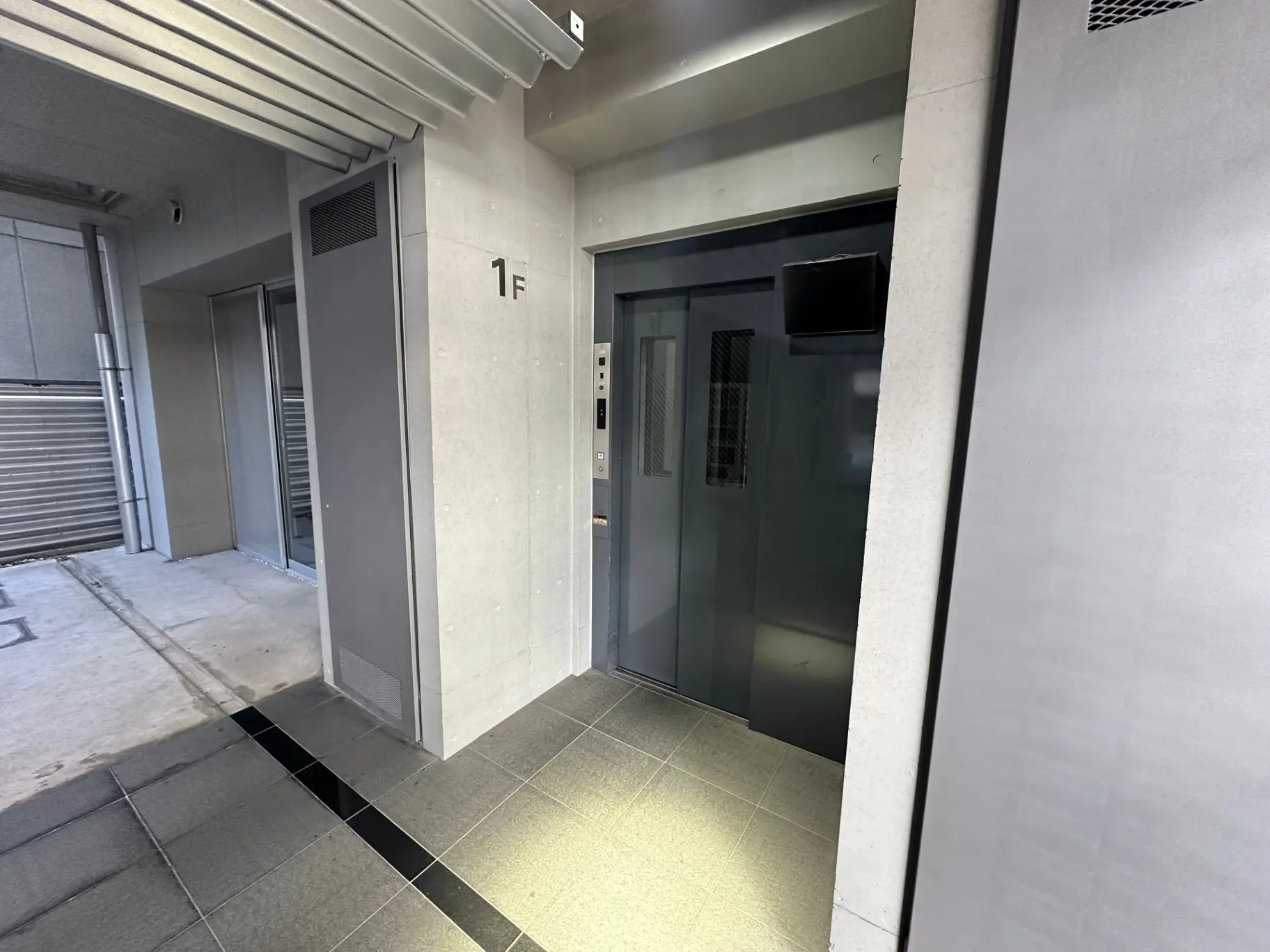 現代的な建物のエントランスにあるエレベーター、清潔感のあるタイル張りの床、1階を示すサイン付き