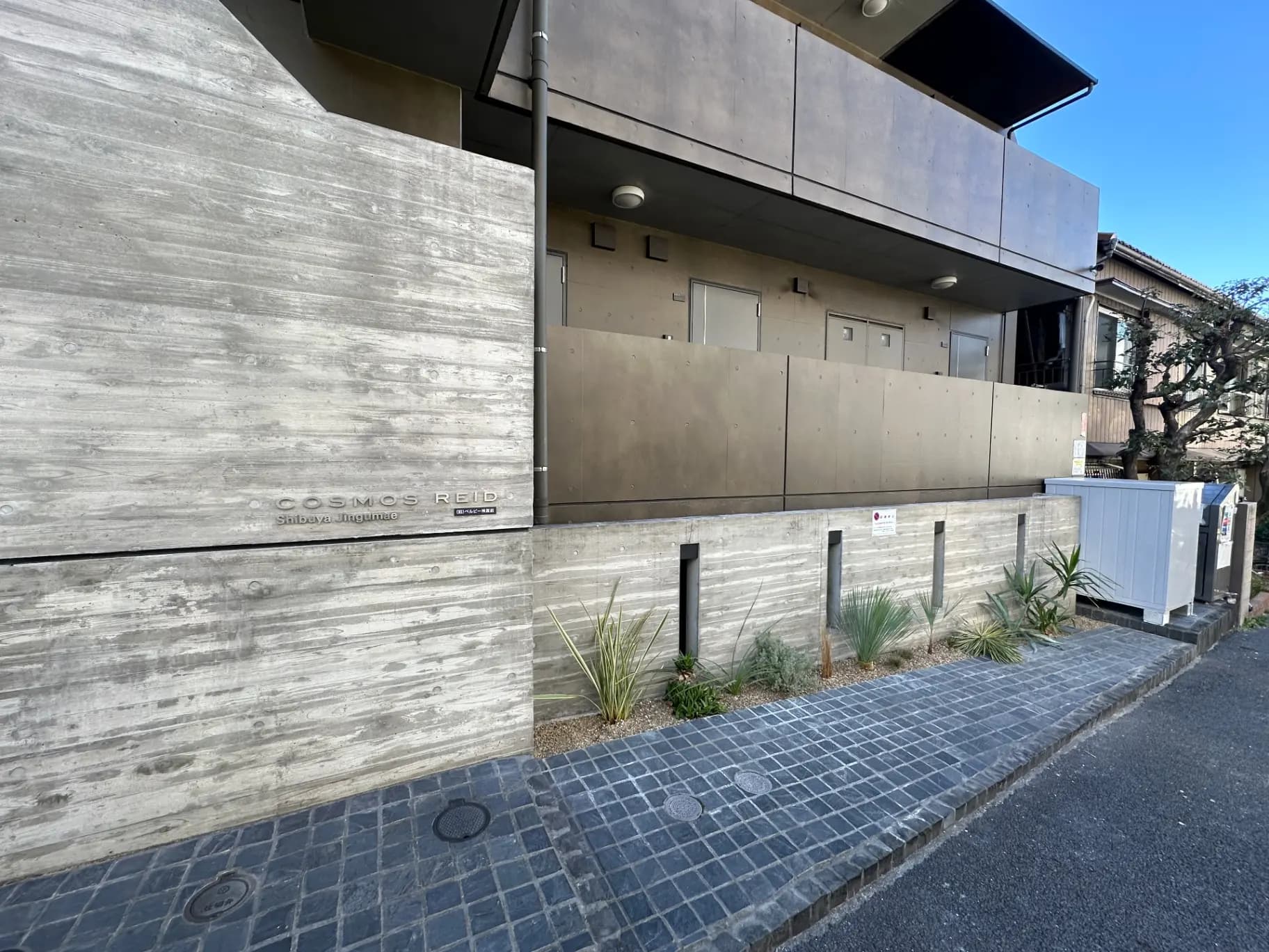 モダンな外観の都市型マンション、コンクリートと金属素材のファサード、植栽付き歩道