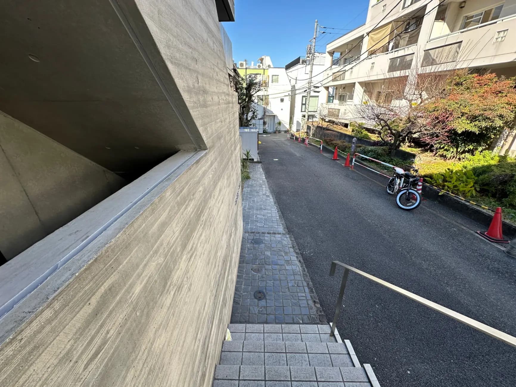 都市のアパートメント複合施設の隣の歩道と緑豊かな植栽、駐輪された自転車が見える風景