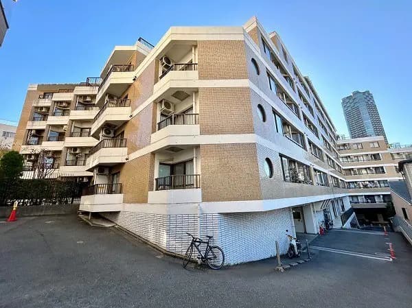 - 都市型マンションの外観、ブロック状のデザインとバルコニー、周囲にはビルが立ち並ぶ景観