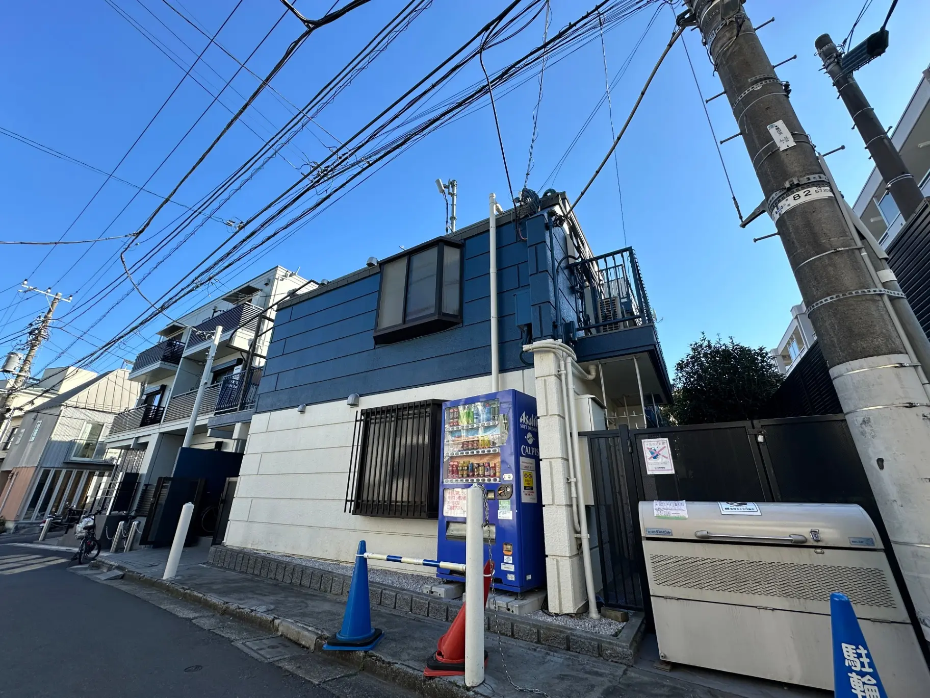 青空の下、電線が通る都市の住宅街、モダンな建物と自動販売機がある風景