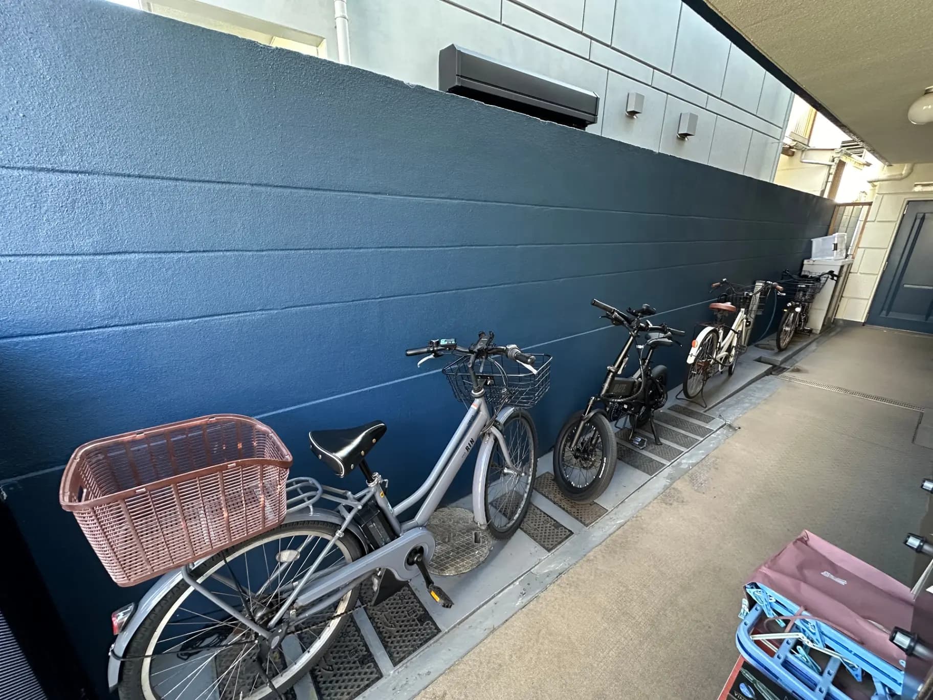 室外の自転車置き場、青い壁面、複数の駐輪された自転車とキャリーカート