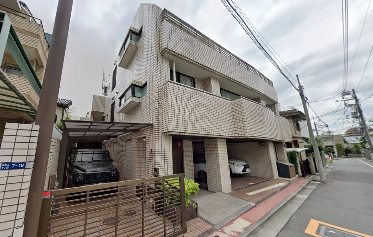 - 現代的なデザインのアパートメントビル、車庫があり、黒いSUVと白い車が駐車されている外観、周囲には電柱と配線が見える通りの風景