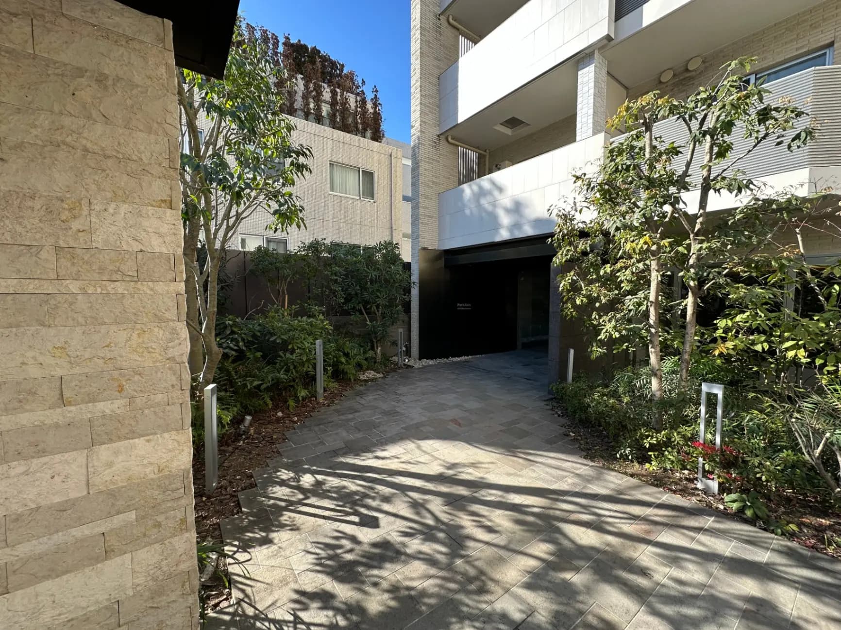 日当たりの良い住宅街のモダンなアパートのエントランス、石畳の歩道と緑豊かな植栽