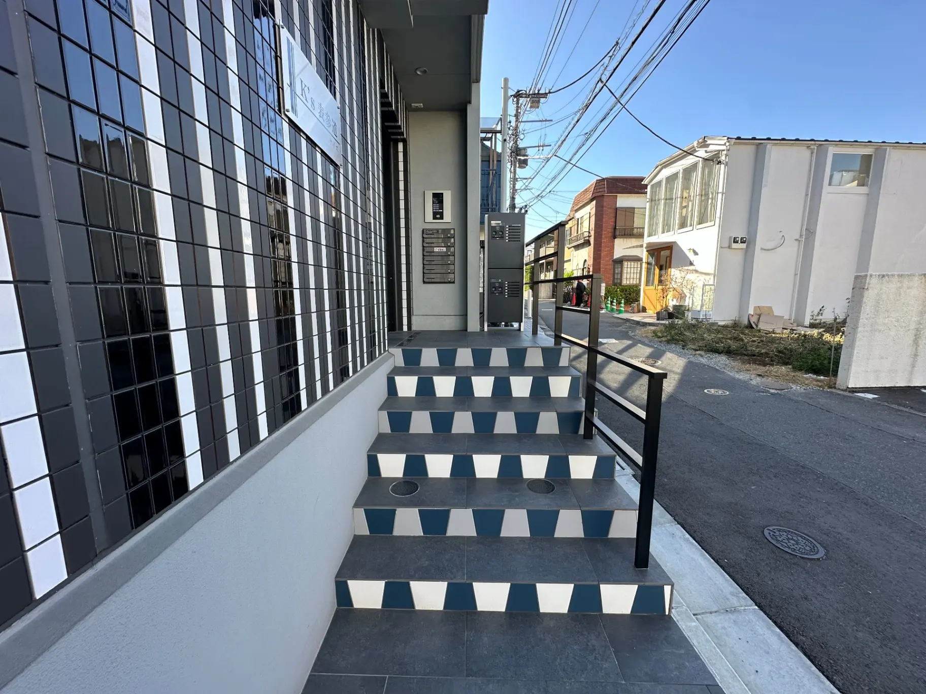 都市の一角に位置するモダンな外観のビルの入口と階段、白と黒のタイルが特徴的なデザイン